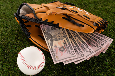 dollar banknotes in baseball glove near ball on green grass, concept