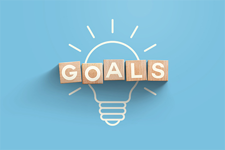 top view of glowing light bulb with goals word made of wooden blocks on blue background