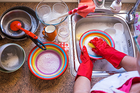 woman washing crockery and cutlery wearing gloves