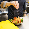 cook sprinkling salt over a bowl of pork and hot peppers while working in the kitchen