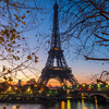 The Eifel tower surrounded by the river greenery and a bridge under a cloudy sky in Paris in the eve