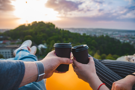 couple laying and enjoying view of sunset over the city. drinking coffee romantic date