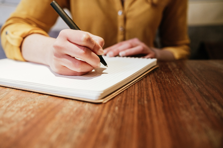 unrecognizable young caucasian woman writing on notebook at a cafe