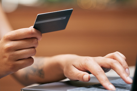 Close up of a woman using a laptop and holding a credit card