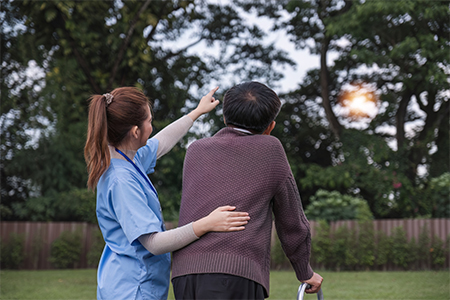 Asian woman caregiver helping senior man walking in nursing home