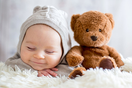 Sweet baby boy in bear overall, sleeping in bed with teddy bear stuffed toys, winter landscape behin