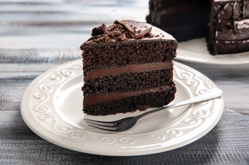 Plate with piece of delicious chocolate cake on wooden table