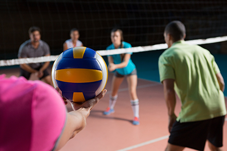 Cropped hand of female player with teammates holding volleyball at court