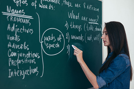 Portrait of woman teacher writing on blackboard in classroom