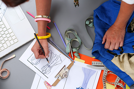 Female fashion designer hands holding drawing pad and pen making sketch of new dress.