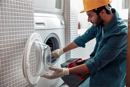 Repairman in worker suit with professional equipment is fixing washing machine in laundry room