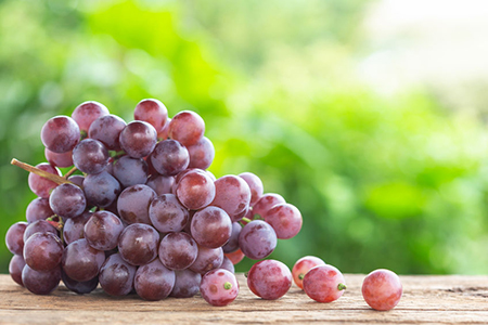 Bunch of ripe red grapes on wooden table with green space blur background