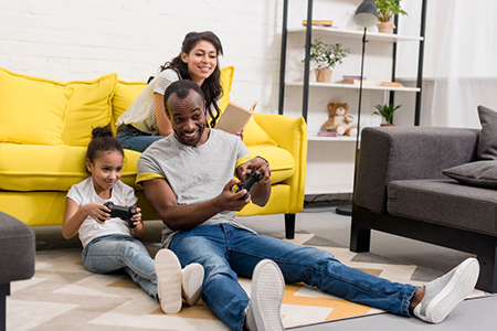 Happy father and daughter playing video games while mother sitting on couch