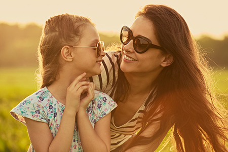 Happy fashion kid girl embracing her mother in trendy sunglasses smiling and looking on each other o