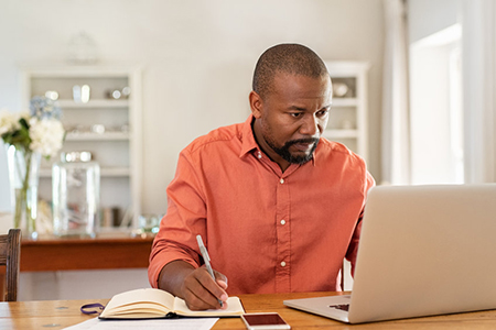 Mature man working on laptop while taking notes. Businessman working at home with computer while wri