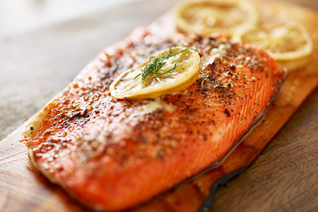 cooked salmon fillet on wooden cedar plank with lemon slices and dill