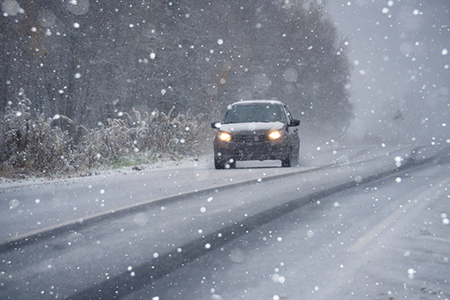 The car is driving on a winter road in a blizzard