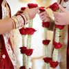 Indian bride and groom in traditional wedding clothes holding red rose flowers.