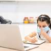 Little girl kid student wearing mask studying online class with laptop at home.