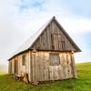 A lonely gray house stands on a wet green meadow among thick gray fog