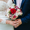 A couple holding bouquet of flowers in wedding dress