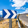 A blue white street sign showing directions next to a road with a scenic background