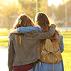 Back view portrait of two affectionate friends walking at sunset in a park