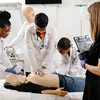 Four international med students practice CPR on a dummy in a classroom