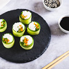 sushi rice, carrots and green onions wrapped in cucumber on a slate board