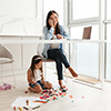 Young asian woman talking on a mobile phone and working on laptop while her little daughter playing 