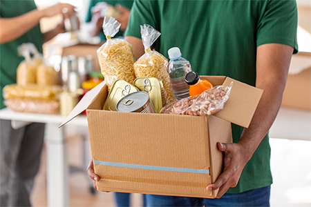 Volunteer holding donation box with food in charity center, closeup