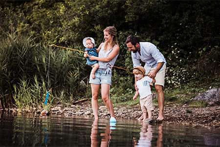A young family with two toddler children spending time outdoors by the river in summer