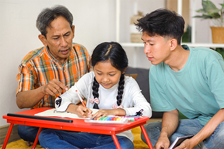 Father And Brother teaching Little Girl Doing Homework On Table While Sitting On The Floor