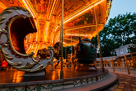 Night view of brightly illuminated merry go round carousel in amusement park, close up