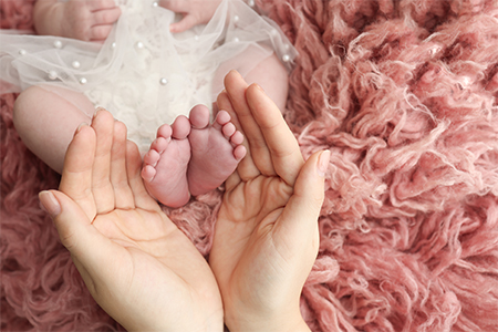 Mother holding the feet of a newborn baby on a background of pink flokati