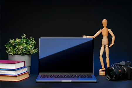 Open laptop with wooden mannequin on table against black background