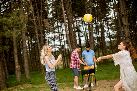 Young women playing volleyball on picnik in spring nature while men preparing grill