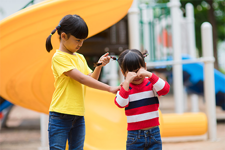 asian little girl pulling her sister's hair in the playground