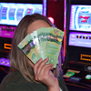Woman covering her face with Canadian cash money in casino beside slot machines
