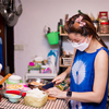 A woman in blue casual pajamas is cooking in the kitchen, wearing a white mask