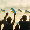 Young people waving ukraininan flags, back view. People with Ukraine flags silhouette, down sky back