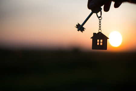 Silhouette of a house figure with a key, a pen with a keychain on the background of the sunset. They