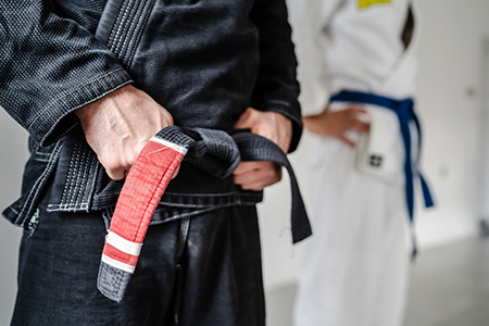 Side view of hand of unknown caucasian man in kimono gi standing while holding black bjj belt brazil