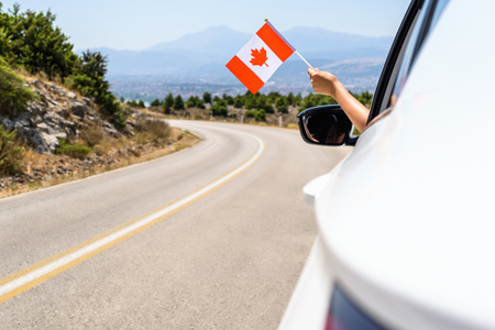 Woman waving flag of Canada from the car window. Travel concept.