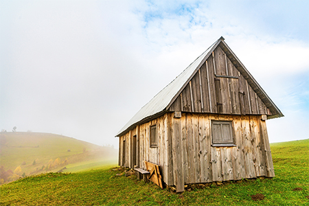 A lonely gray house stands on a wet green meadow among thick gray fog