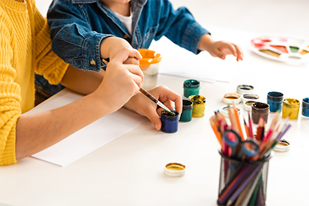 cropped view of brother and sister sitting at table and drawing with paints together