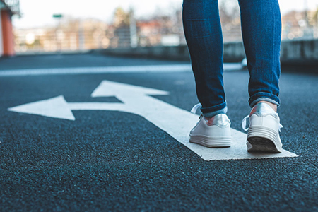 Make decision which way to go. Walking on directional sign on asphalt road. Female legs wearing jean