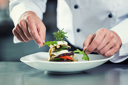 Chef in Restaurant garnishing vegetable dish, crop on hands, filtered image