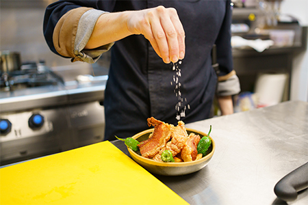 cook sprinkling salt over a bowl of pork and hot peppers while working in the kitchen