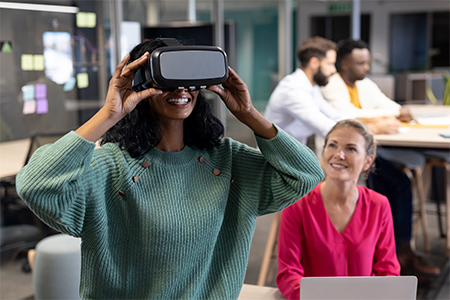 Smiling african american businesswoman wearing vr simulator by caucasian colleague at workplace